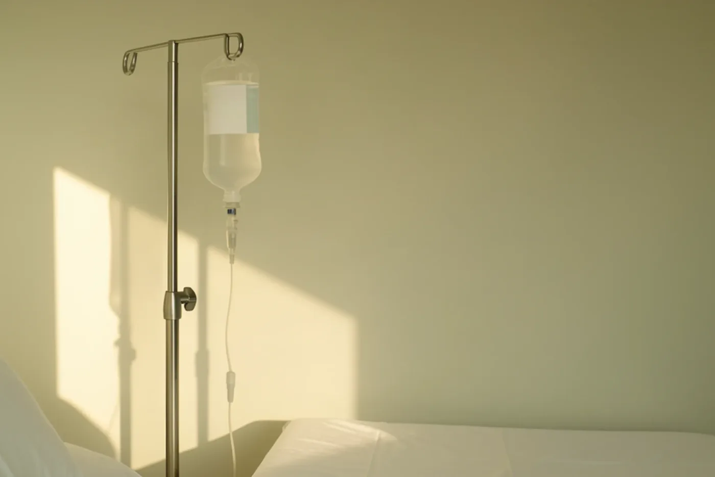 An IV drip stand beside a clinical bed in soft morning light