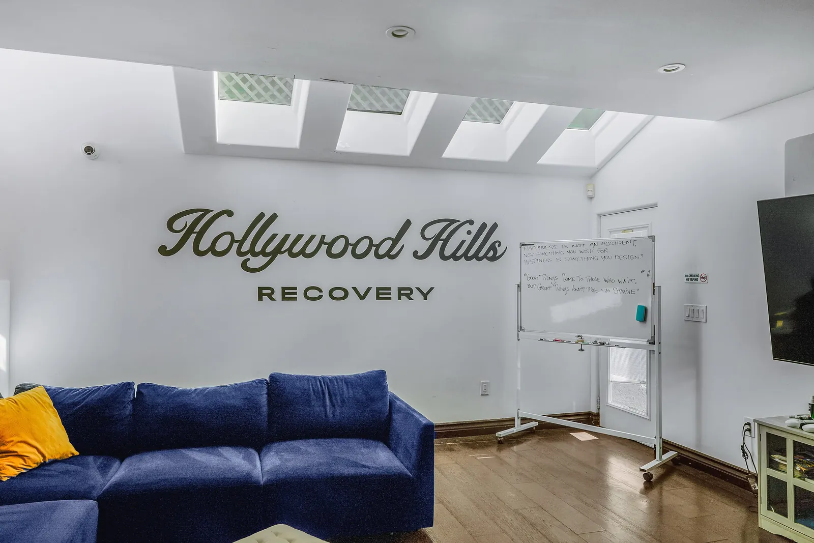Bright group room with blue sofas, skylights and the Hollywood Hills Recovery name on the wall