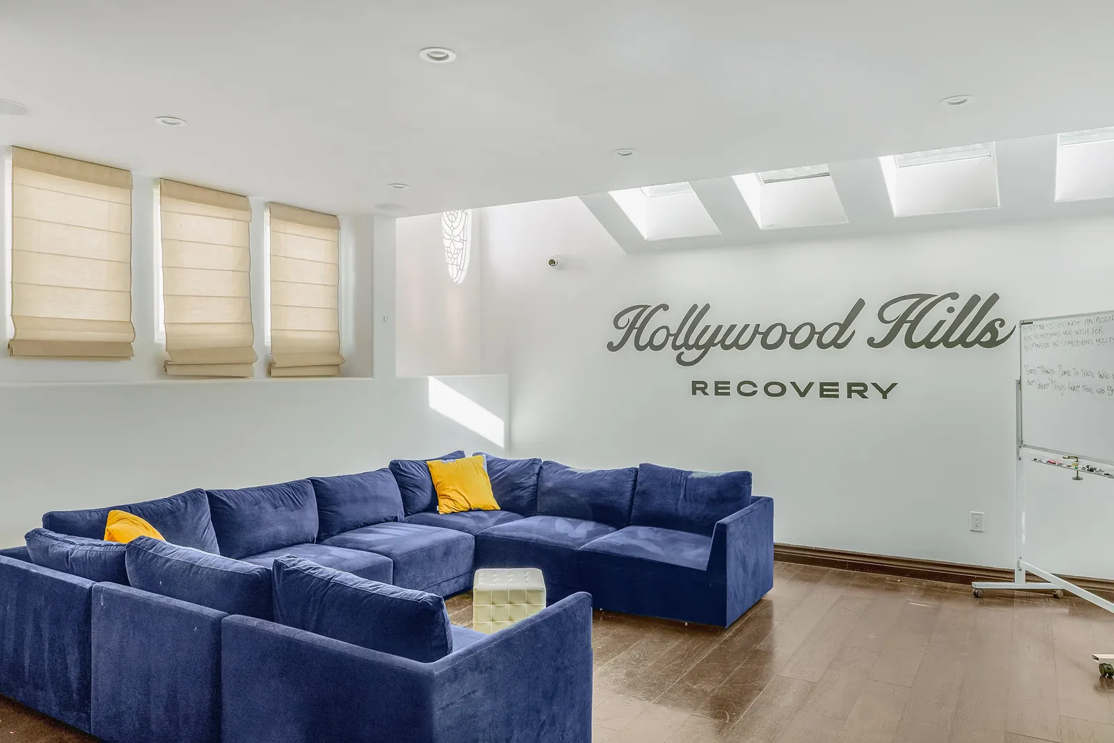 Group room with a large blue sectional, shuttered windows and the Hollywood Hills Recovery name on the wall