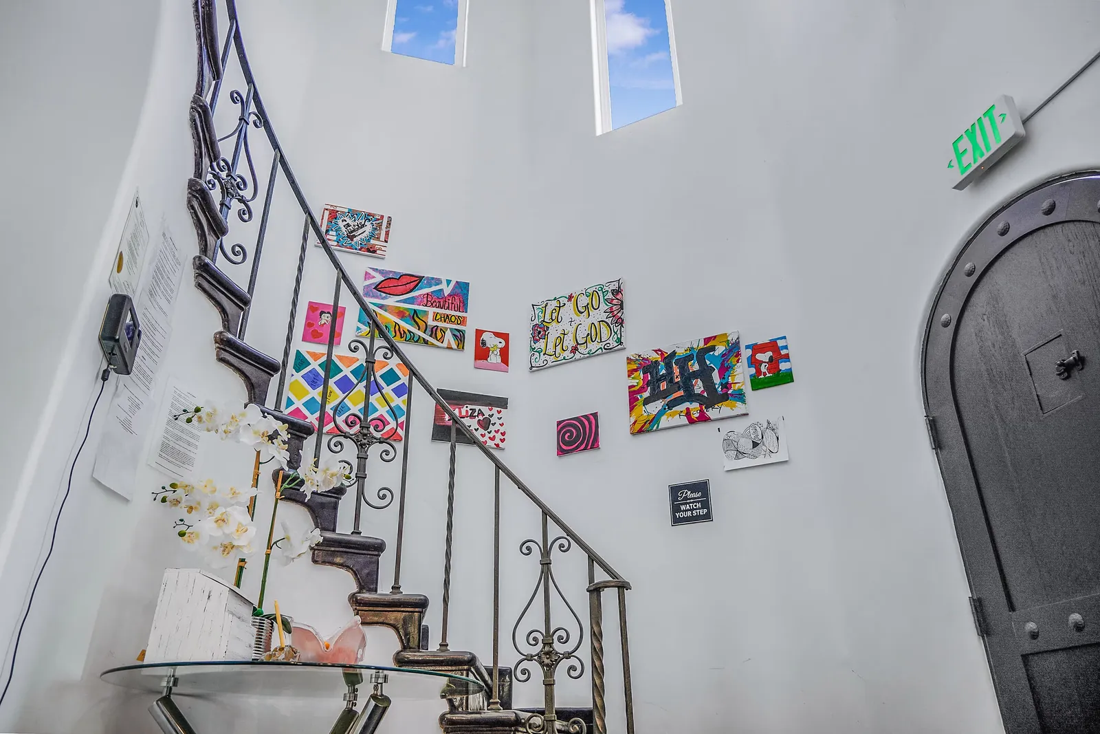 Staircase hung with small artworks, beside a tall arched wooden door