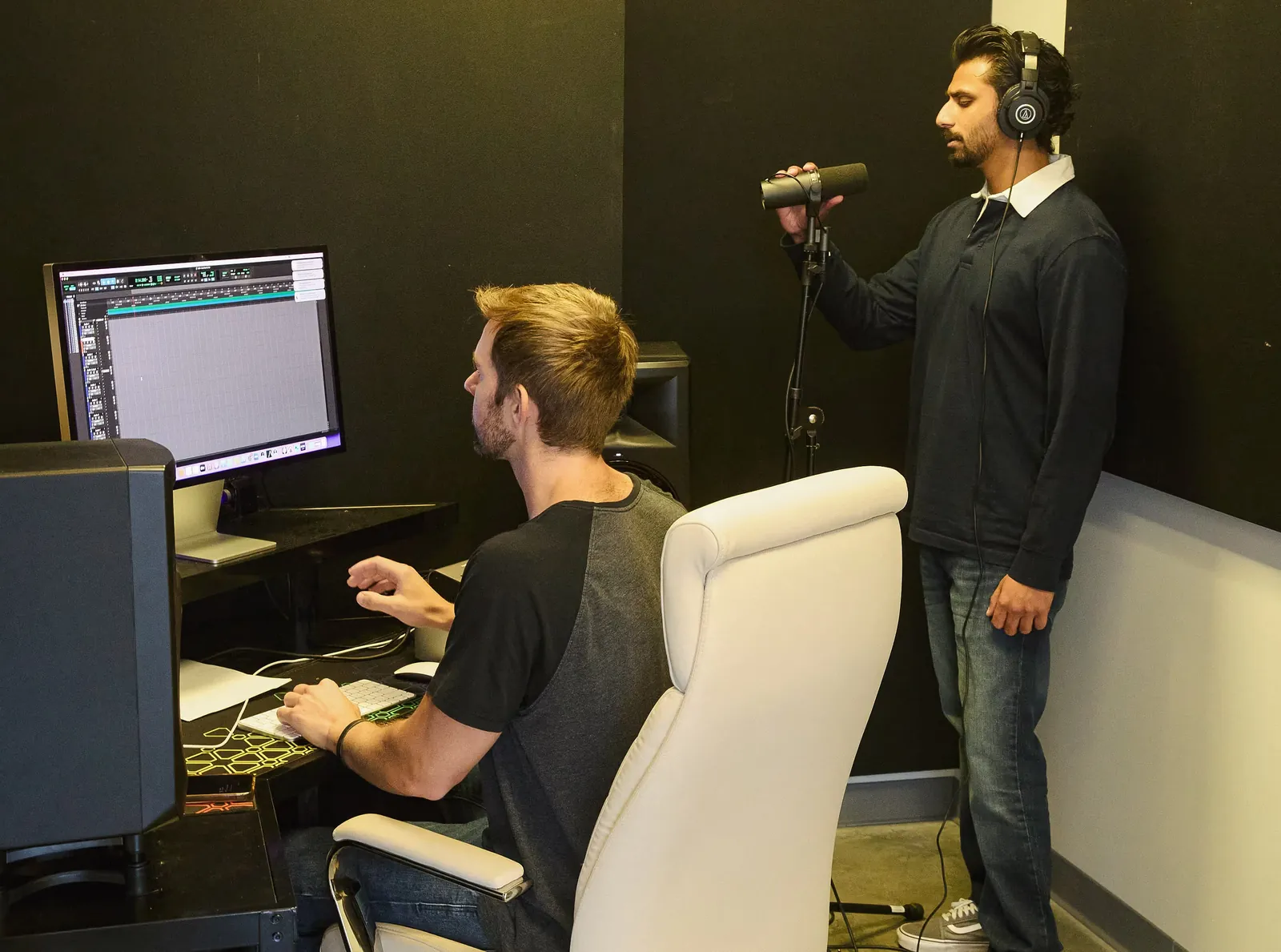 A recording booth with a microphone and an engineer at the desk