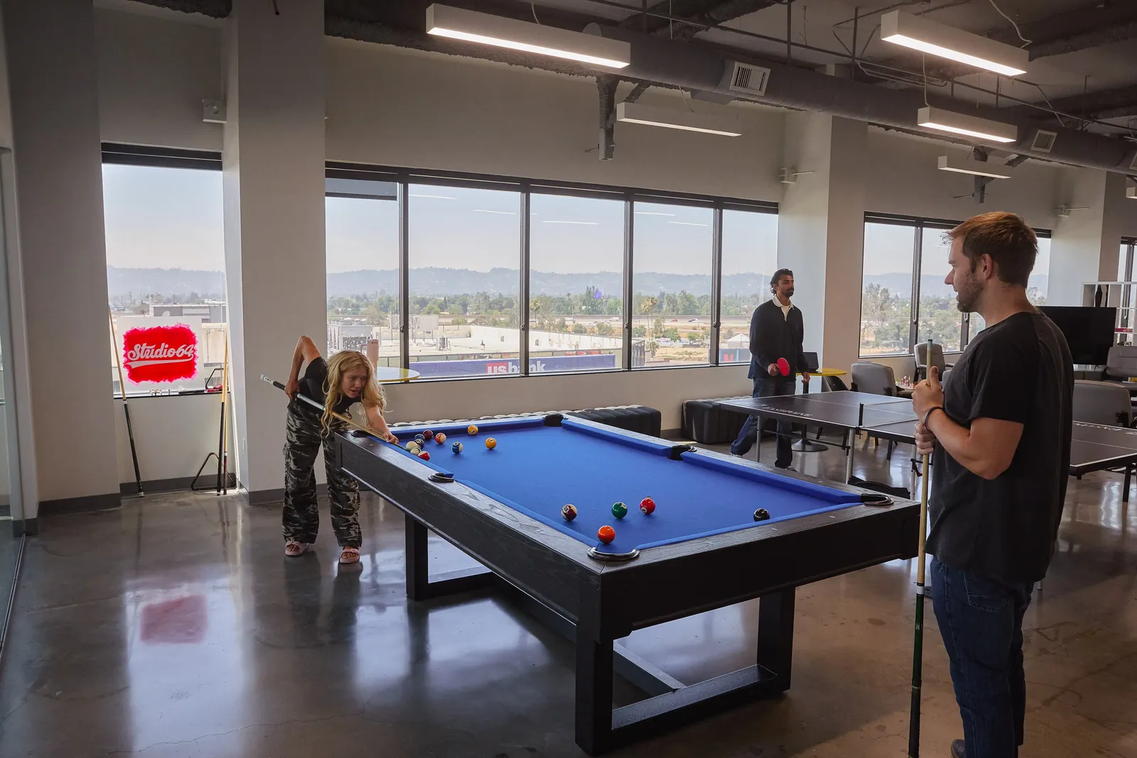 Open room with a pool table and table tennis, people playing by the windows