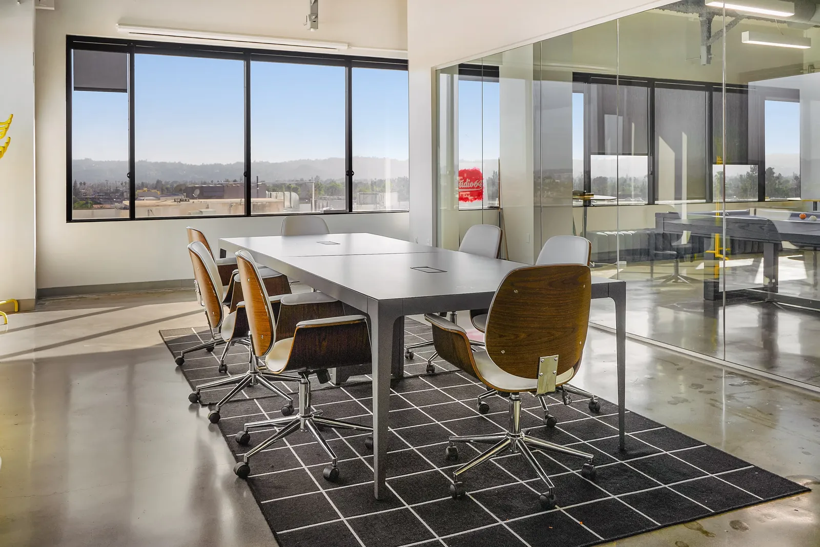 Meeting room with a long table and chairs against a wall of city-facing windows
