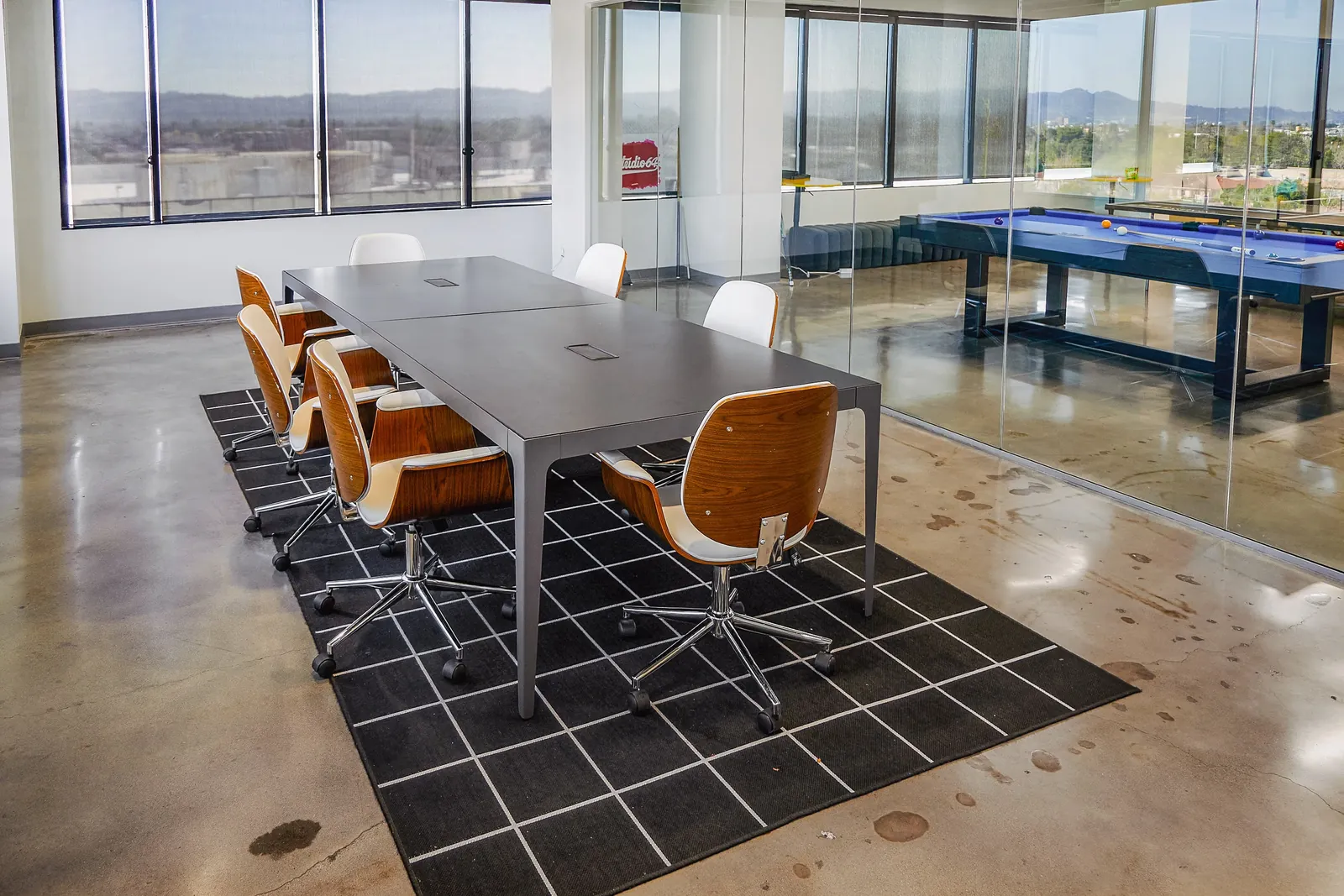 Conference table and chairs, with a games area visible beyond the glass partition