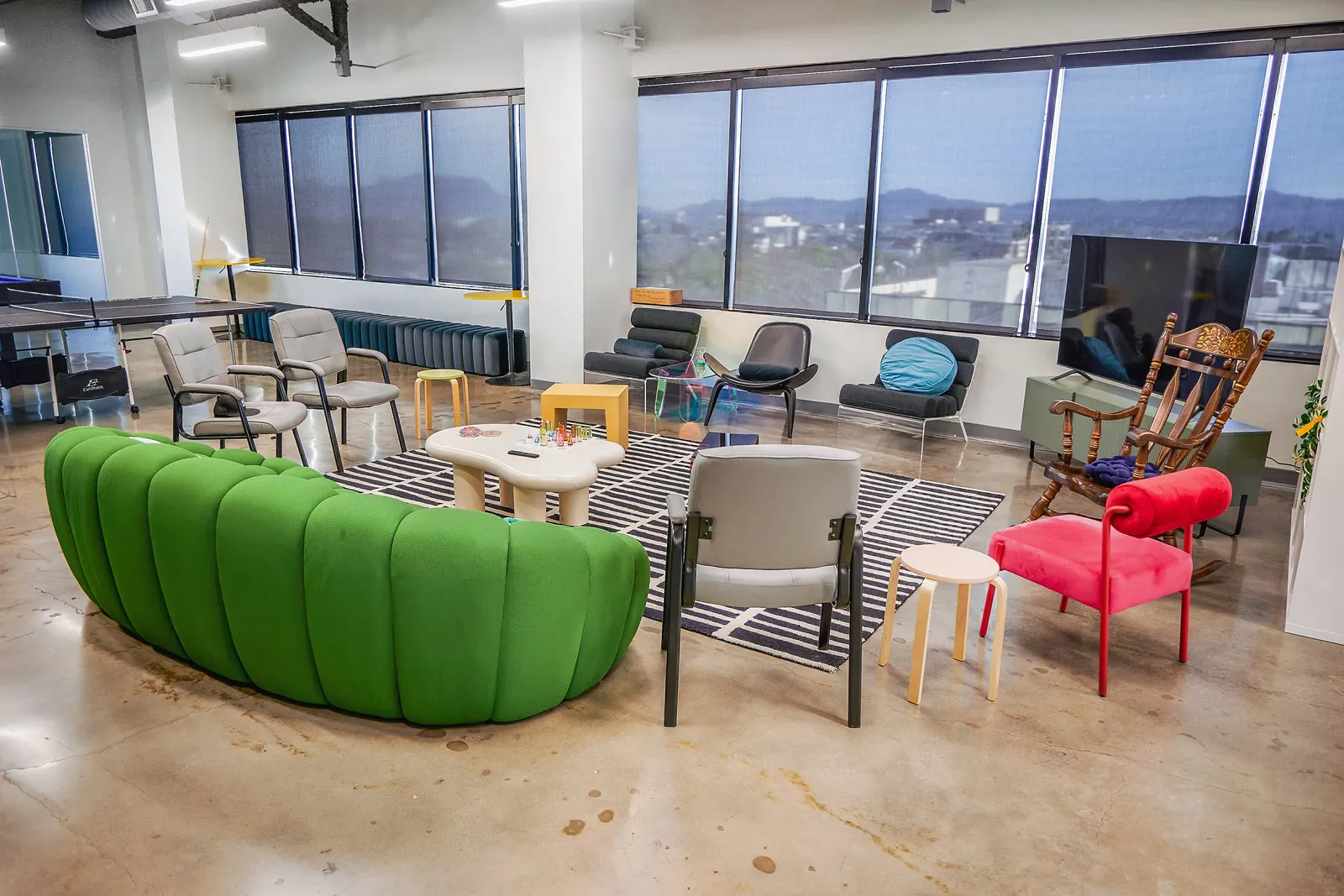 Open lounge with a green sofa, armchairs and tall windows