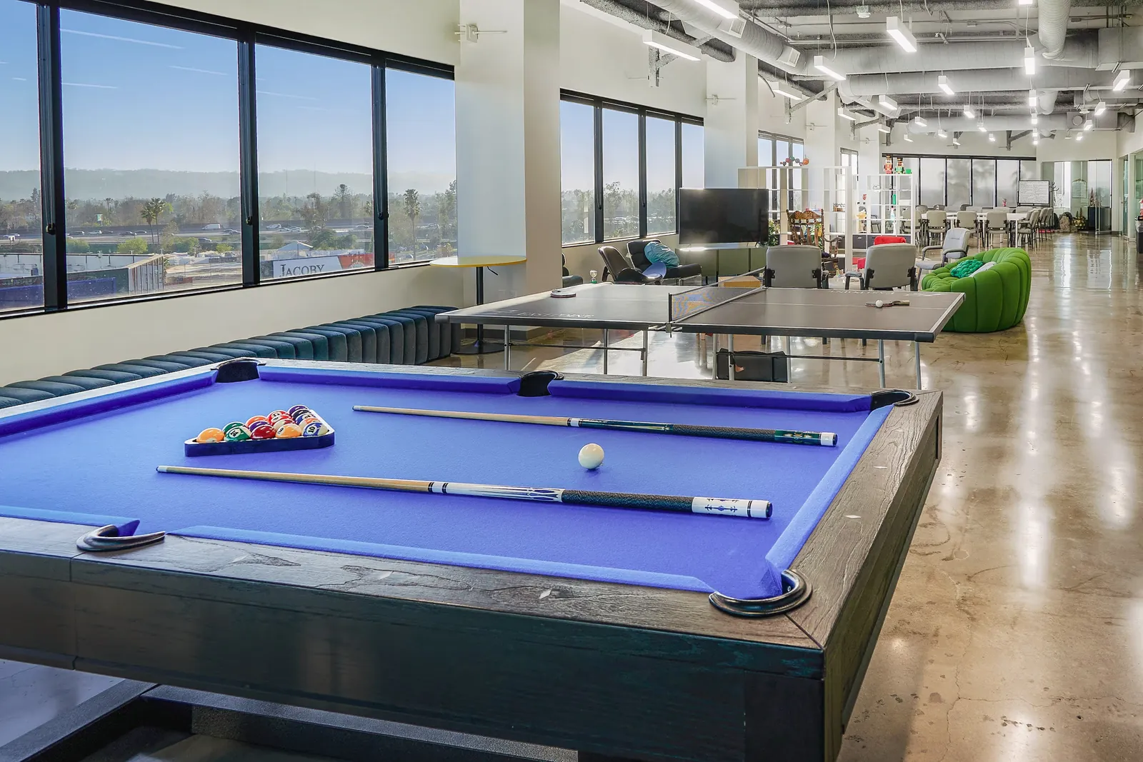 Blue-topped pool table beside a wall of windows
