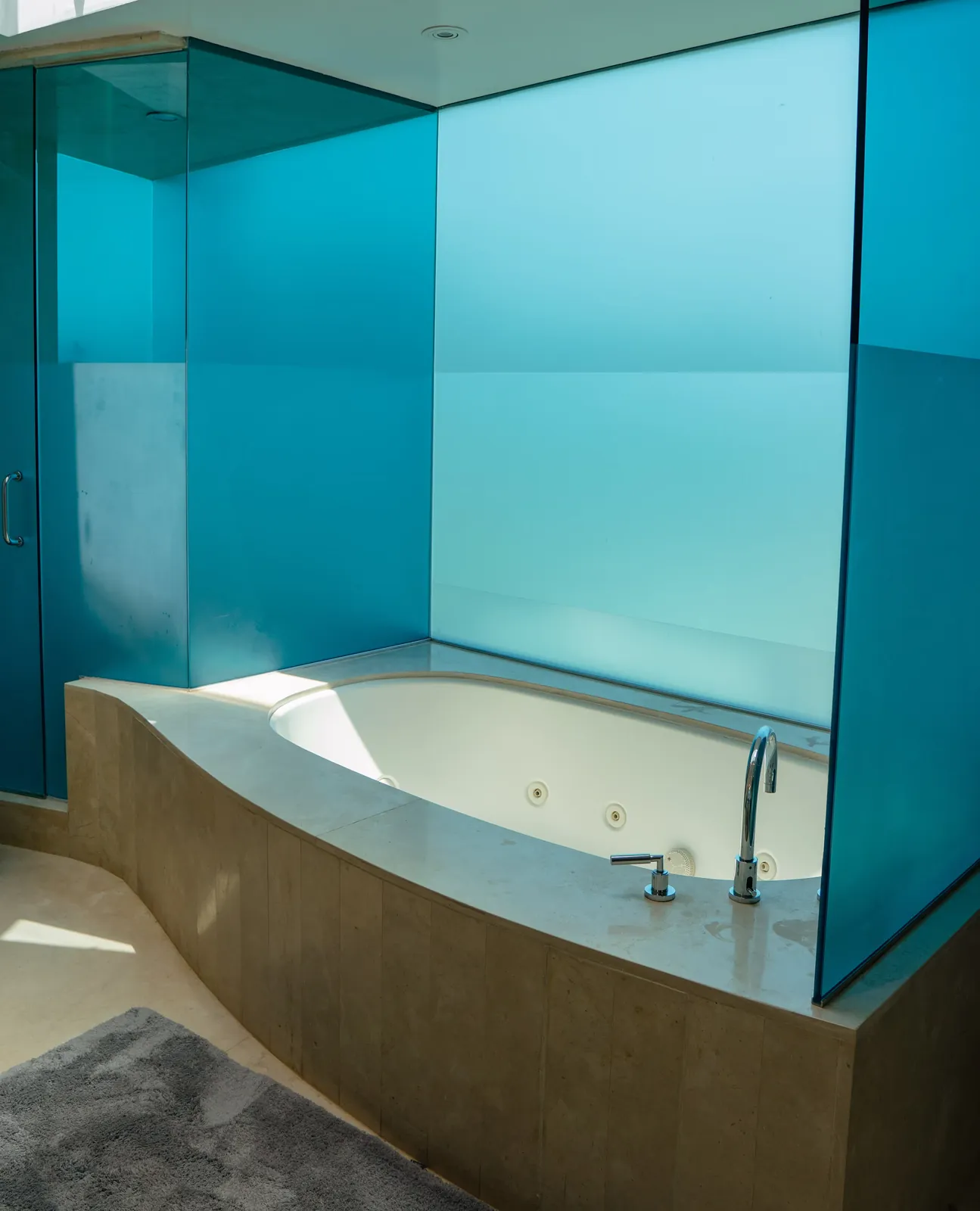 Jacuzzi tub set into stone, screened by a panel of blue glass