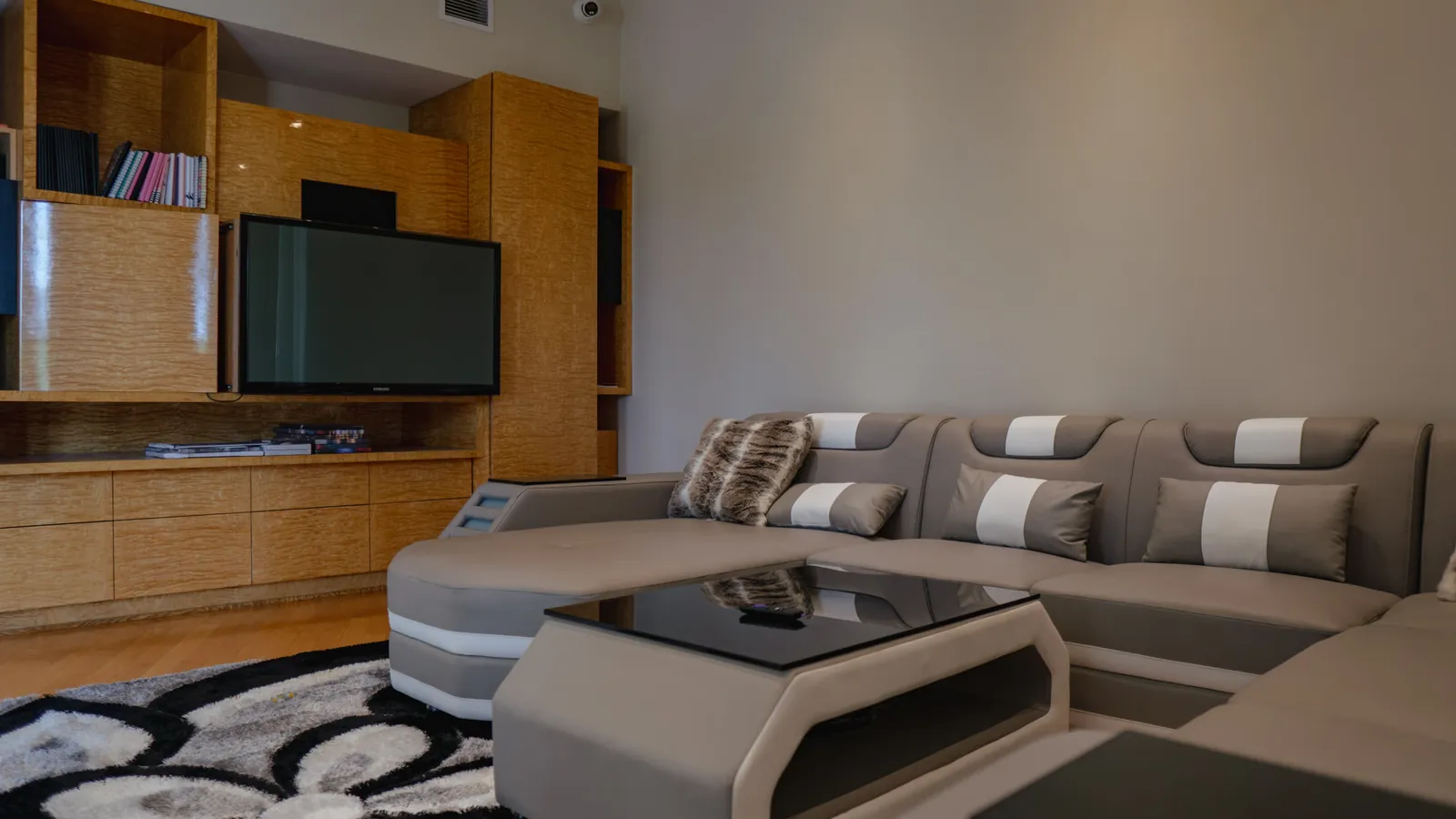 Living area with a curved sectional sofa, wall-mounted television and patterned rug