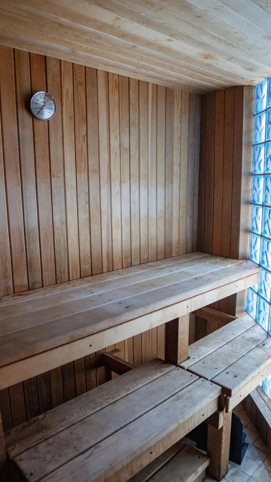 Cedar sauna with a tiered bench, wall clock and a glass block window