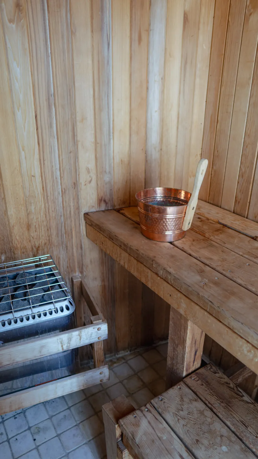 Sauna interior with a wooden bench and a copper bucket and ladle