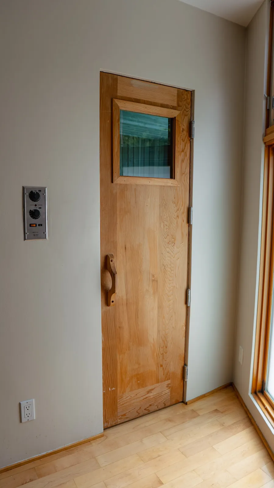Sauna door in pale wood with a viewing window and wall controls