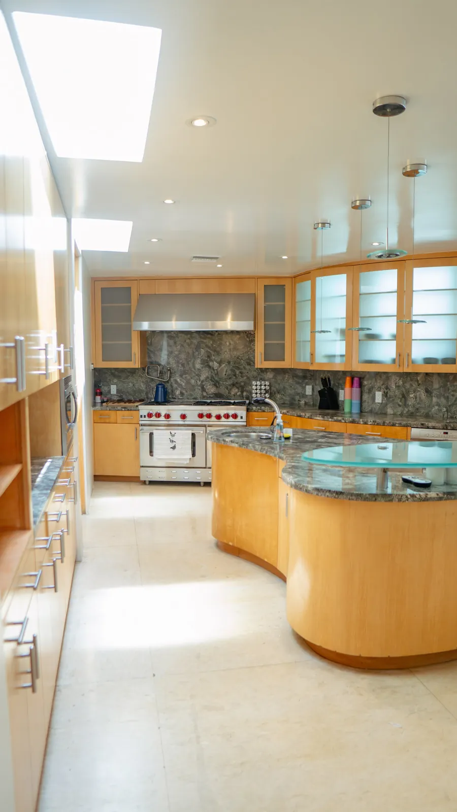 Kitchen lit by a long skylight, with a curved island and glass-fronted cabinets