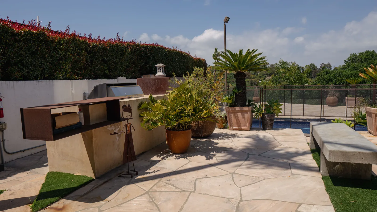 Outdoor kitchen and paved terrace beside the pool, with potted planting