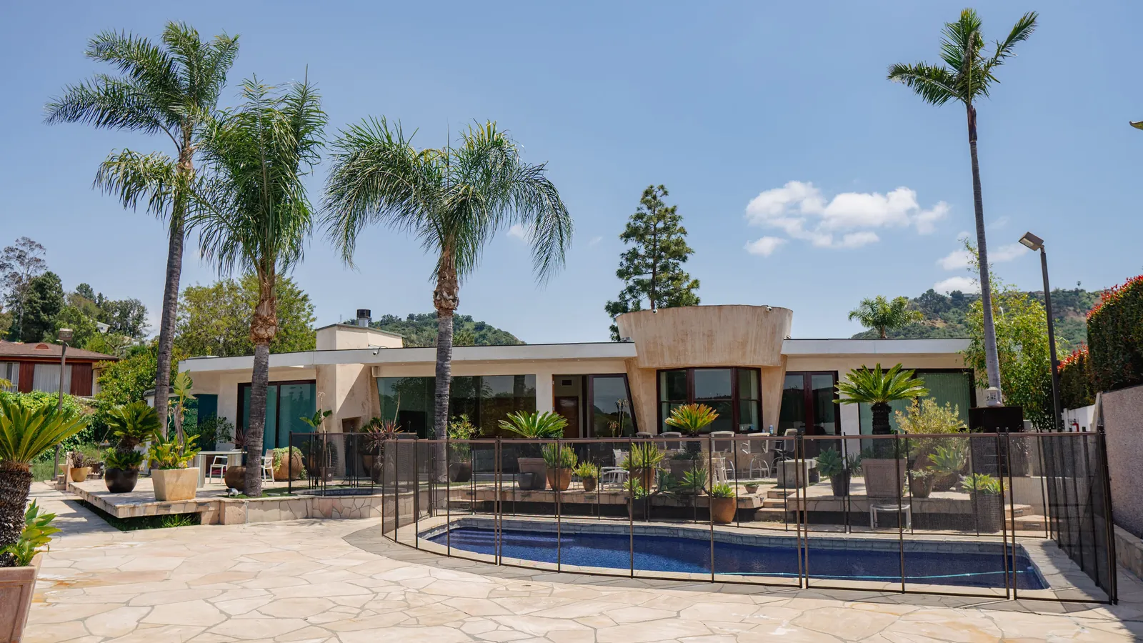 Swimming pool and flagstone terrace in front of a single-storey house, framed by palms